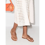 Woman wearing Tory Burch Miller Sandals in brown leather with Double T logo, flat rubber sole, and branded insole, paired with a summer dress.